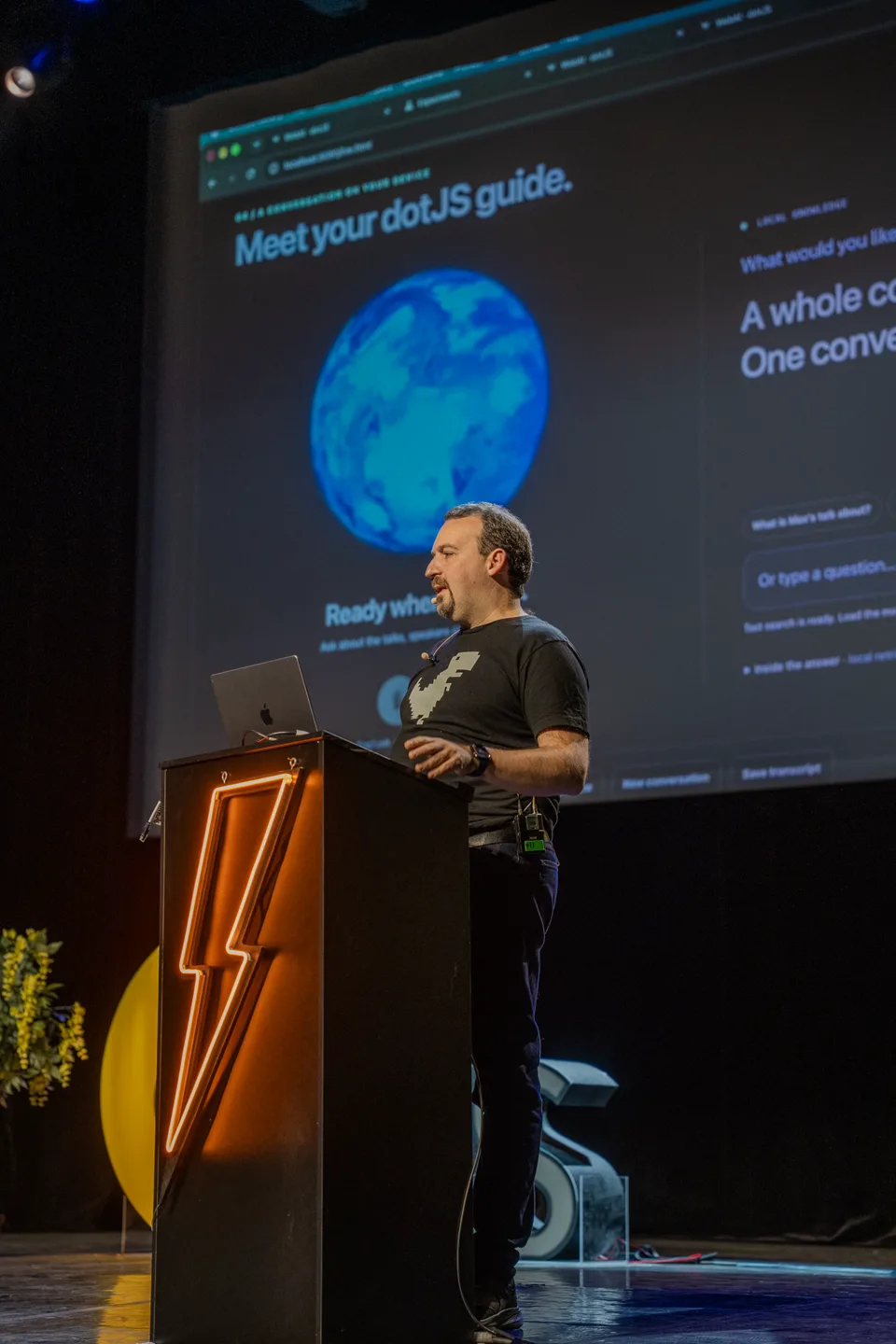 Intervenant à dotJS derrière un pupitre éclairé d’un éclair orange